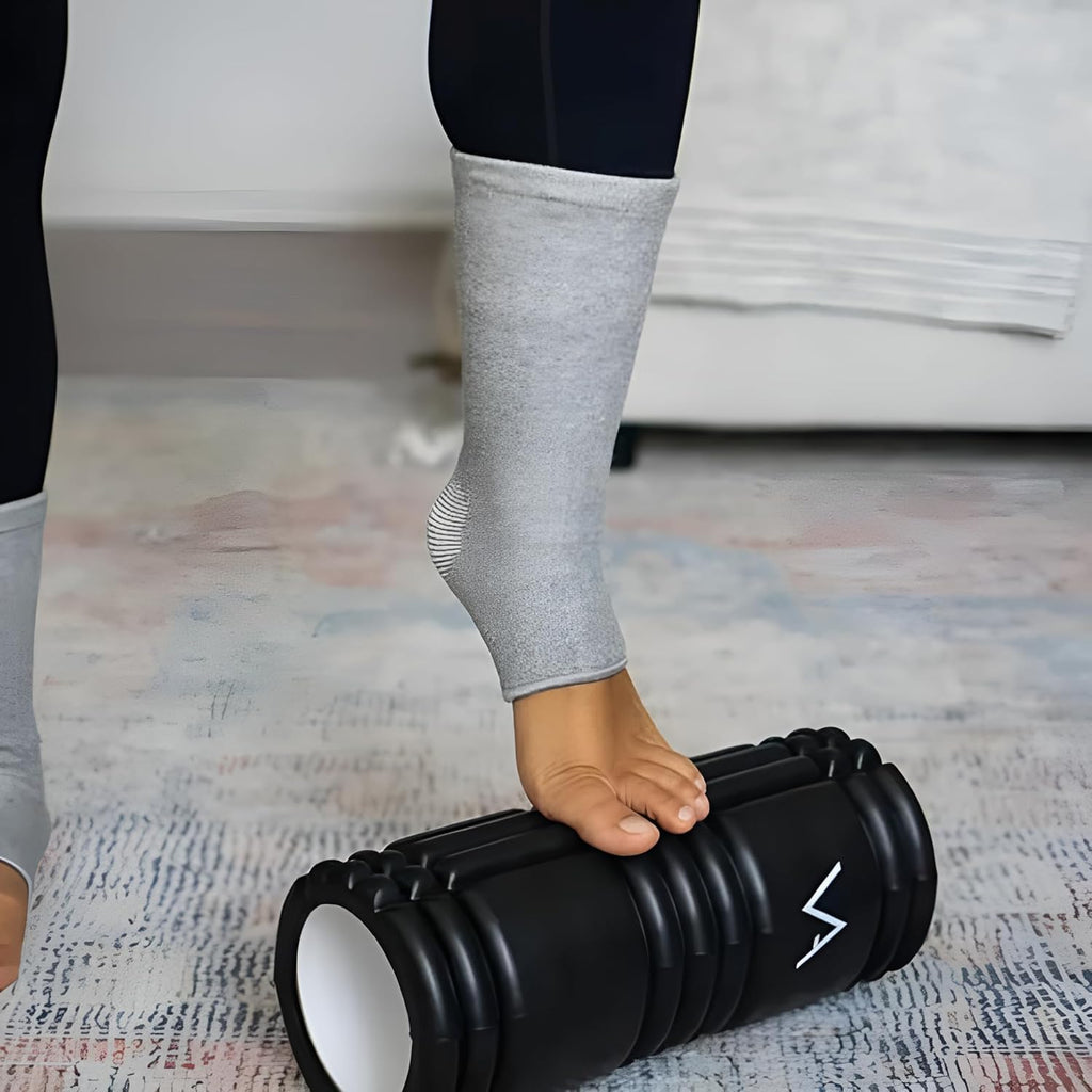 Person using black foam roller, wearing grey ankle brace, on textured rug indoors