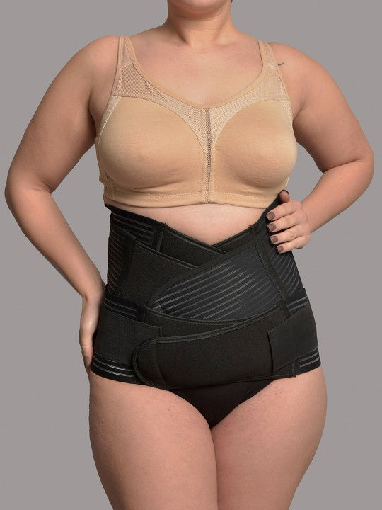 Woman wearing black 3-in-1 postnatal shapewear and beige bra against grey background